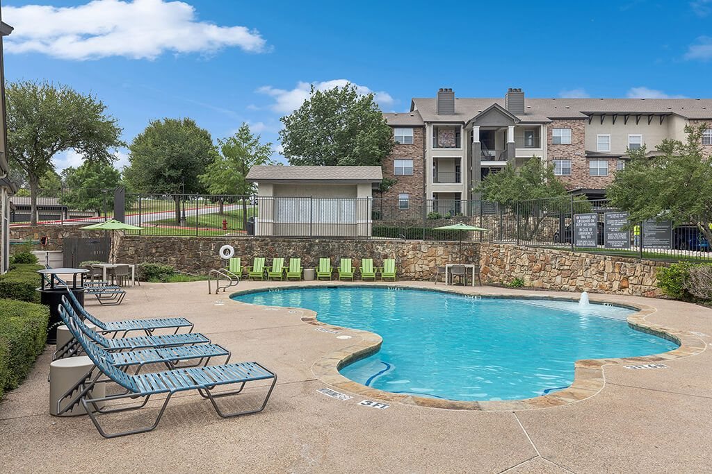 A swimming pool surrounded by a stone wall and lounge chairs.